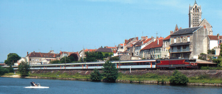 À Dormans, depuis la Marne, les occupants d’un pédalo admirent le passage de l’express Corail 1004 Strasbourg - Paris‑Est, au crochet de la BB 15009, filant en direction de la capitale (30 mai 1982 ; L. Chanteloup).