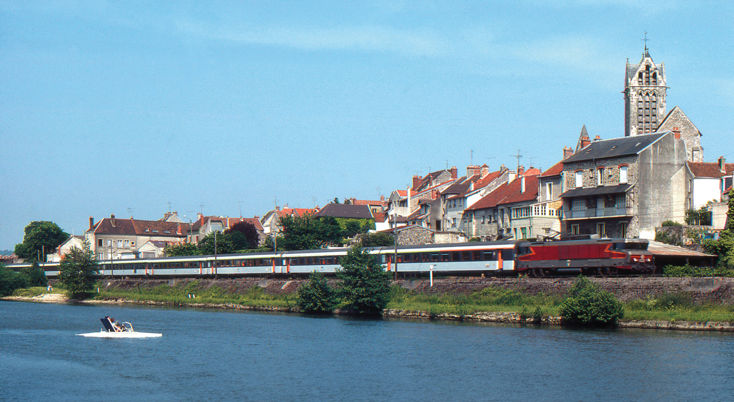 À Dormans, depuis la Marne, les occupants d’un pédalo admirent le passage de l’express Corail 1004 Strasbourg - Paris‑Est, au crochet de la BB 15009, filant en direction de la capitale (30 mai 1982 ; L. Chanteloup).