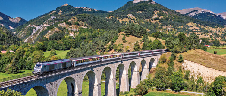 Peu après le village des Lussettes, dans la descente du col dans une zone limitée à 40 km/h par manque d’entretien, le train test Grenoble - Briançon est aperçu au franchissement du viaduc des Fauries (longueur 185 m), peu avant d’aborder la gare de Lus-la-Croix-Haute (7 septembre 2025 ; P.-L. Espinasse).