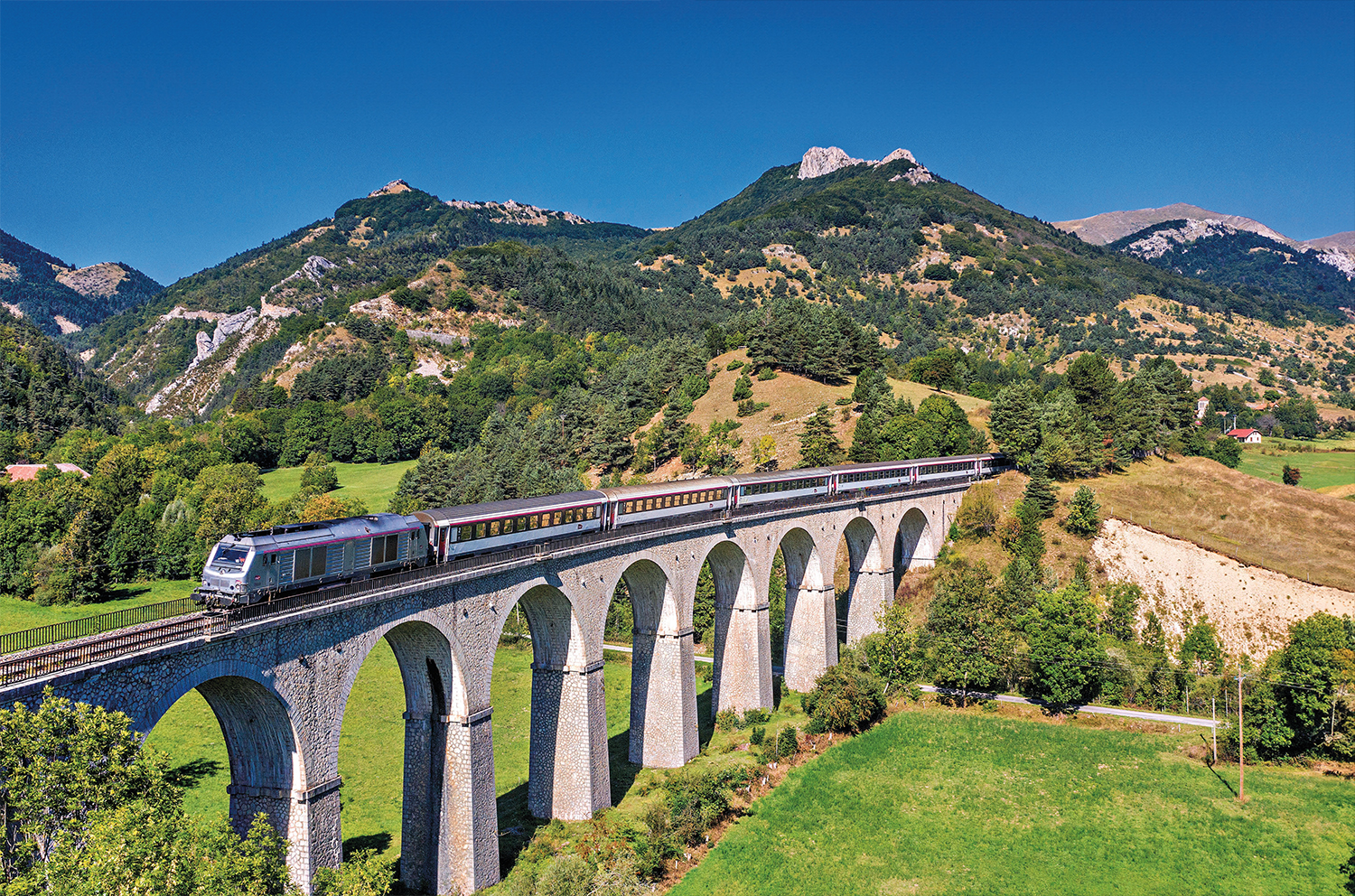 Peu après le village des Lussettes, dans la descente du col dans une zone limitée à 40 km/h par manque d’entretien, le train test Grenoble - Briançon est aperçu au franchissement du viaduc des Fauries (longueur 185 m), peu avant d’aborder la gare de Lus-la-Croix-Haute (7 septembre 2025 ; P.-L. Espinasse).