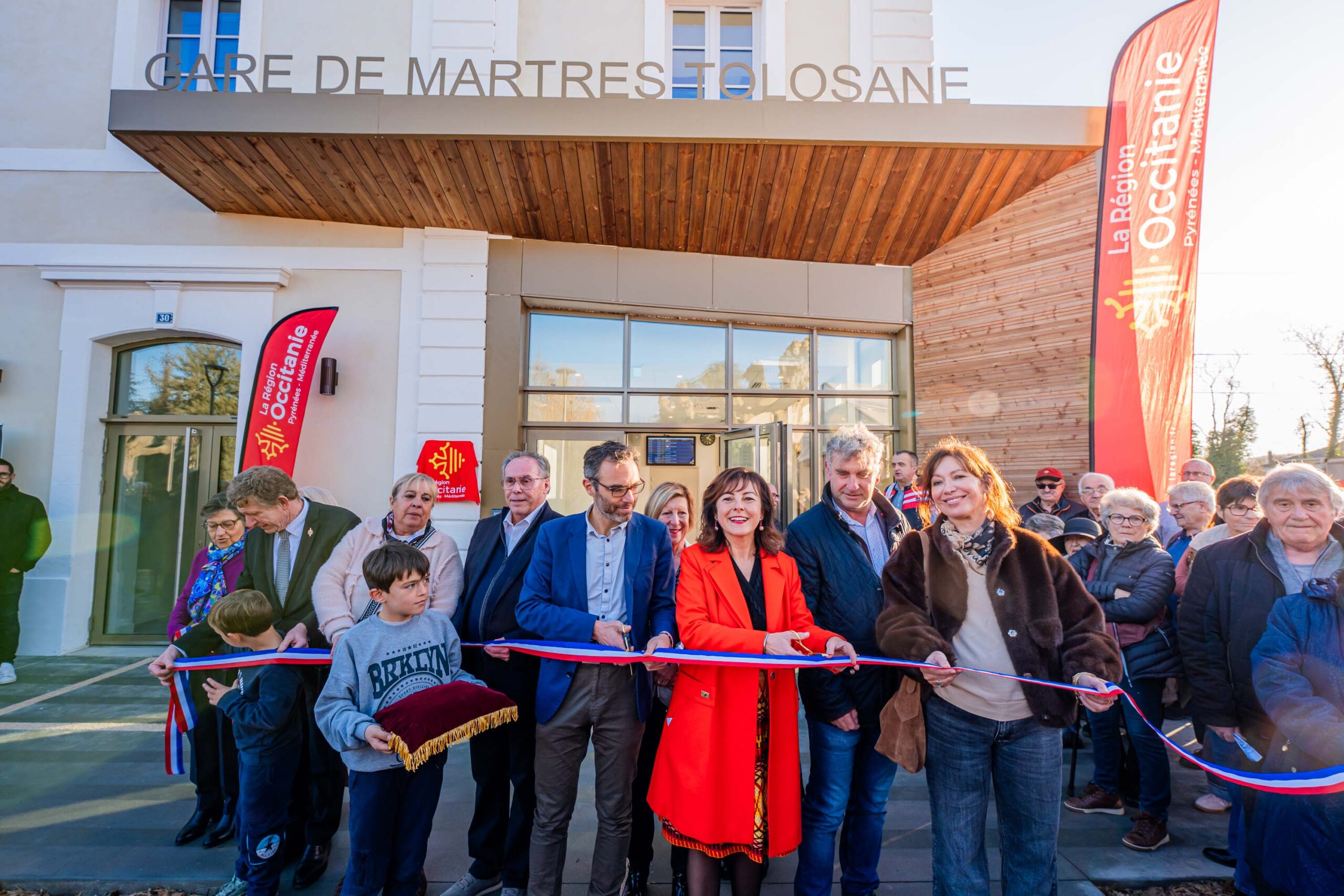 Légende : Carole Delga (en rouge) coupe le ruban de l’inauguration de la gare de Martres-Tolosane le 13 décembre 2025 (© Région Occitanie).