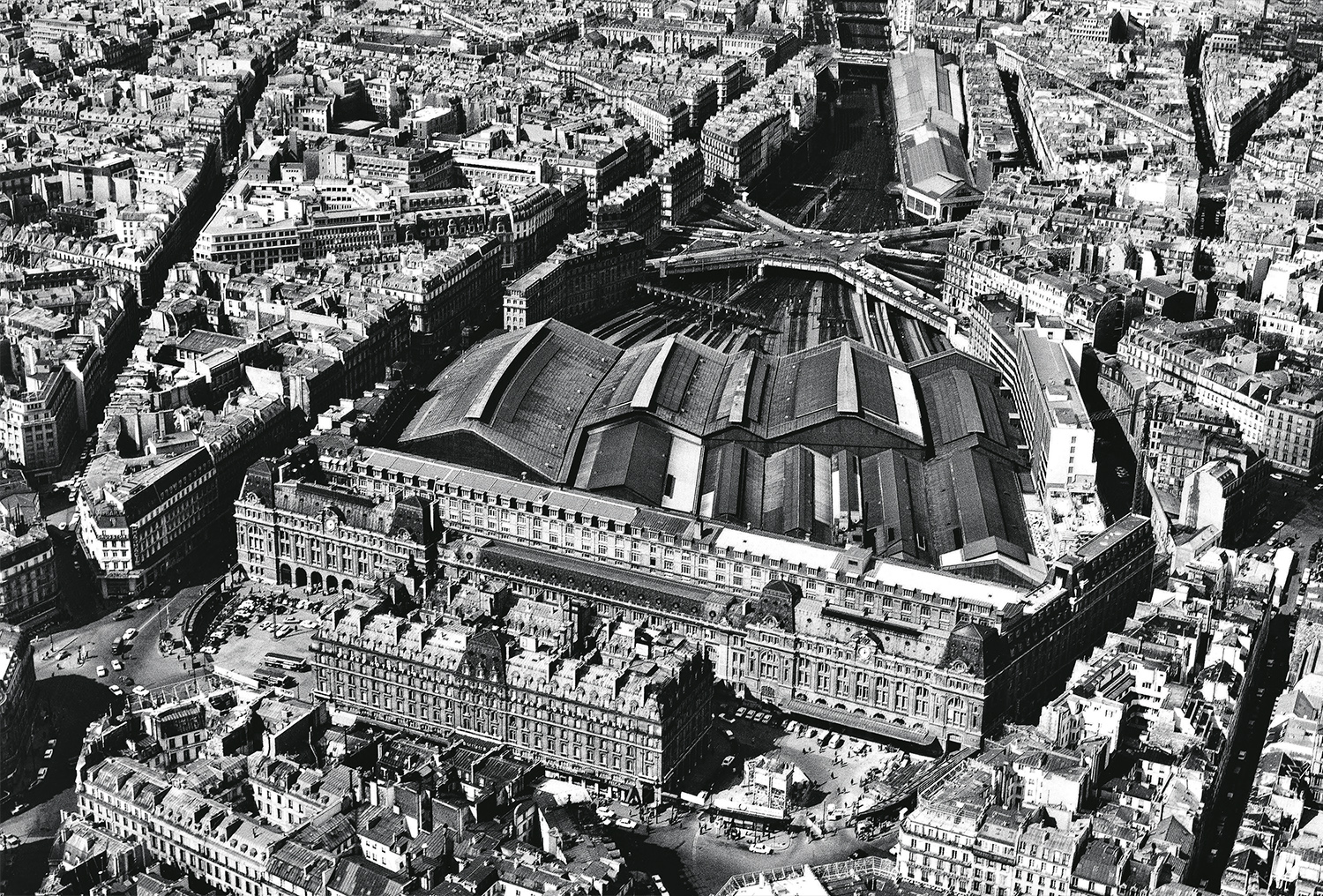 Paris-Saint-Lazare en 1970. L’on note les cours de Rome et du Havre, situées de part et d’autre de l’hôtel Concorde, encore fermées à l’époque par des grilles et des enfilades de petites boutiques ; l’on remarque également la grande disparité des halles couvrant les voies, résultant des agrandissements successifs de la gare ; en haut de l’image, l’on distingue l’unique souterrain subsistant de la batterie d’ouvrages qui composaient l’ancien tunnel des Batignolles, conservé pour supporter la rue de Rome (R. Henrard/LVDR).