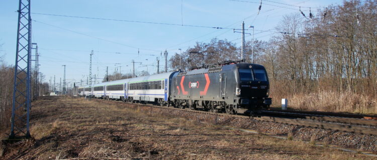 Le train EC 135 Leipzig Hbf – Wrocław Głowny, composé de la Vectron 5370 055-3 louée par PKP IC à la Rosco Cargounit remorquant une rame de voitures de PKP IC, vient de quitter à 11 h 55 la gare d’Elsterwerda (15 décembre 2025).
