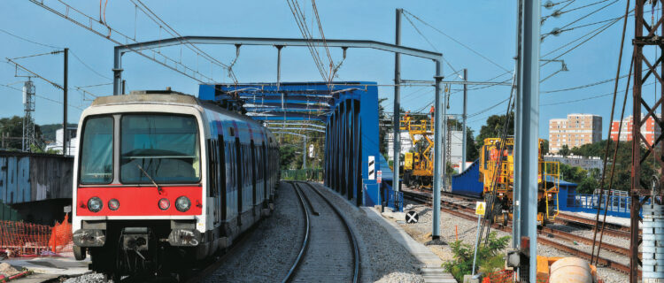 Un exemple de chantier nécessité par l’arrivée du nouveau matériel MI 20 : le remplacement du pont de Chartres, vu ici à Massy le 23 août 2023 avec une rame MI 79 en direction de Massy-Palaiseau ; à droite, les travaux de finitions sur l’ouvrage SNCF du RER C dit pont de Gallardon.