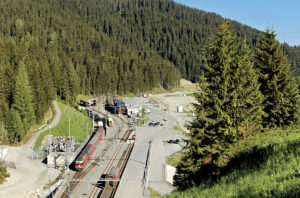 Depuis le portail du tunnel de la Vereina, vue sur le terminal de Klosters-Selfranga. Le train de voyageurs visible vient de quitter le tunnel de Zugwald et va disparaître dans celui de la Vereina (Bernhard Studer ; 11 juin 2006).