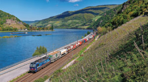 Une Vectron bleu SBB Cargo International sur un train pour l’Italie passe Assmannshausen, sur la rive droite du Rhin (23 avril 2024 ; F. Pobez).